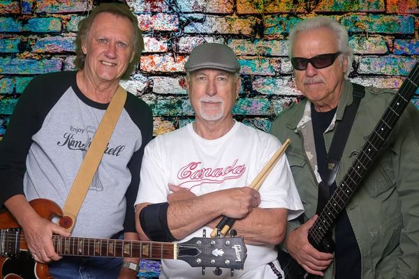 Giv'R — three-piece Edmonton band posed in front of a colourful painted brick wall