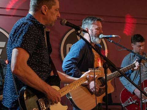 Full band shot from audience perspective at venue with red ambient lighting