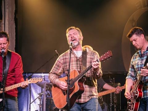 The Threads performing on a proper stage under warm spotlights, three guitarists visible